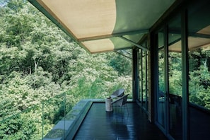 A modern outdoor deck with glass walls, a wooden floor, and a seating area with chairs. - zuowang hotel (Chengdu)