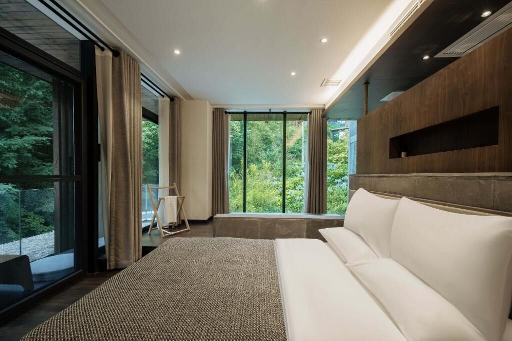A modern bedroom with a large bed, a view of greenery, and a built-in shelf.