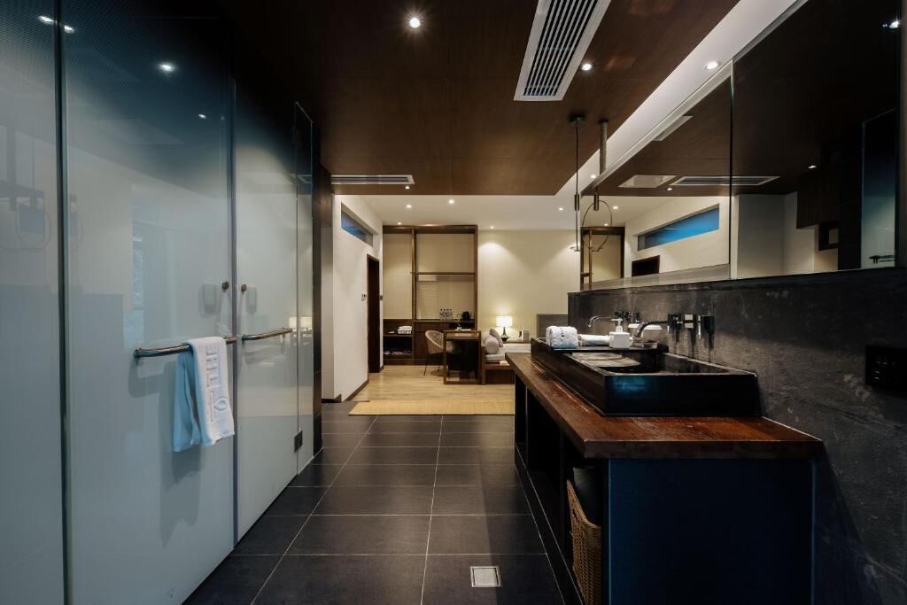 A modern bathroom with a large mirror, dark tiles, and a wooden countertop.
