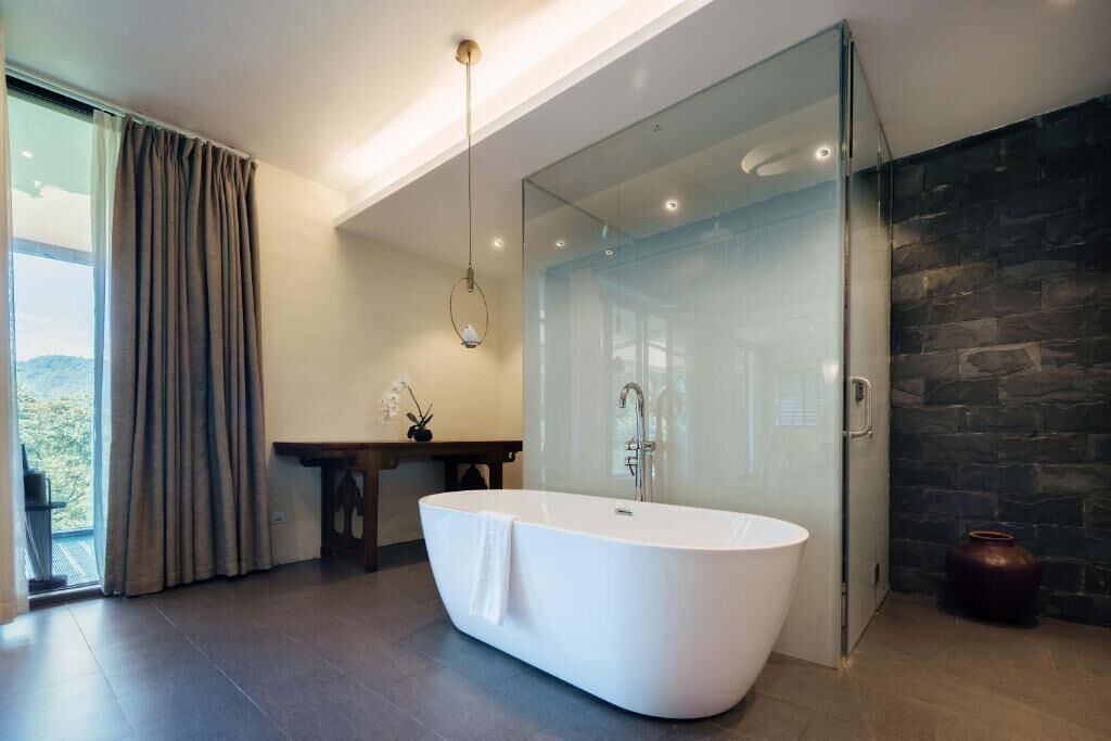 A modern bathroom with a freestanding bathtub, a glass shower enclosure, and a view of the outdoors.