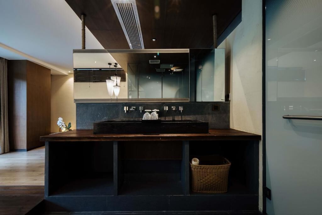 A modern bathroom with a large mirror, dark countertop, and a small wicker basket.