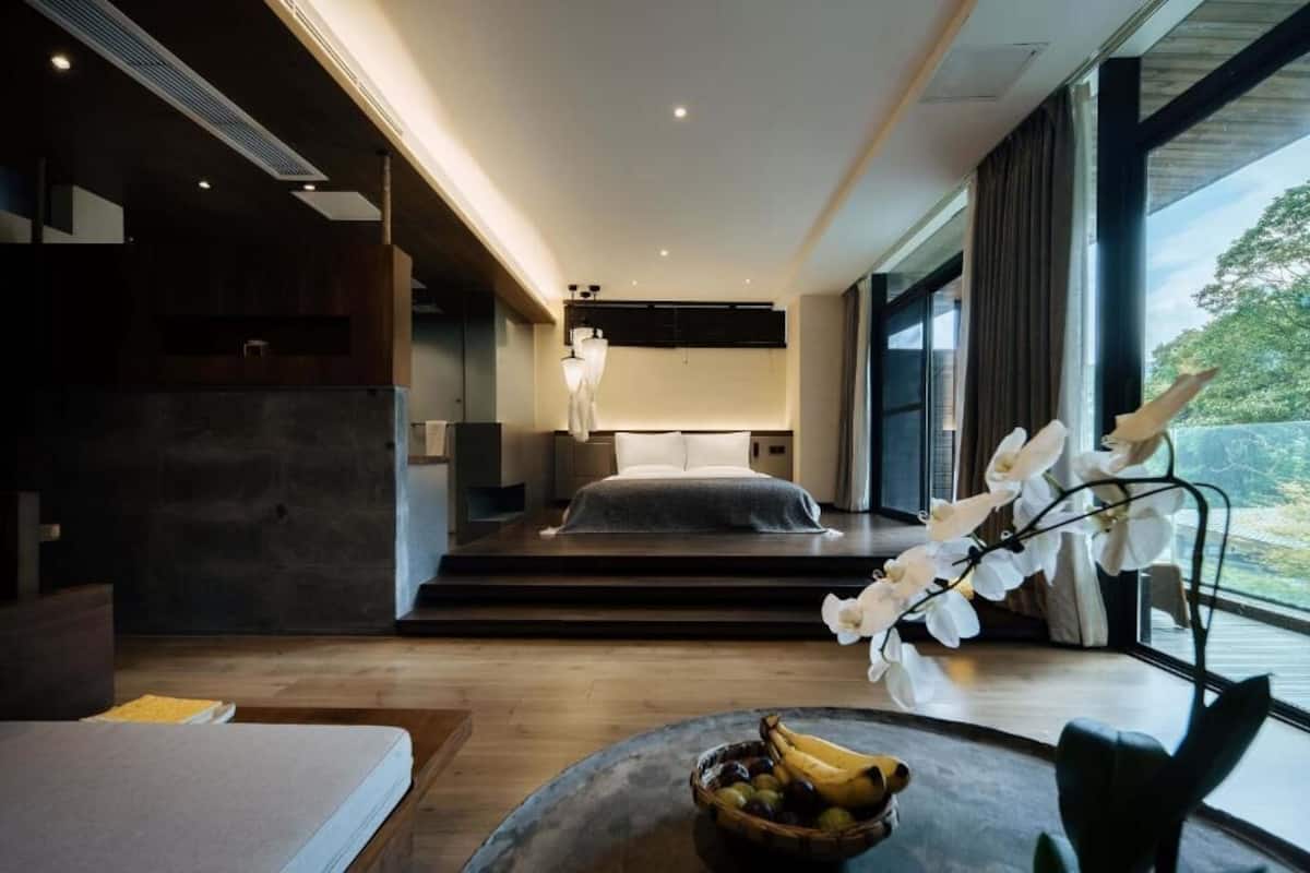 A modern bedroom with a bed, bedside table, and a view of the outdoors.