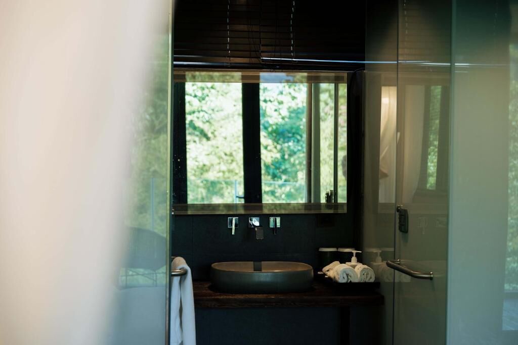 A modern bathroom with a round sink, a large mirror, and a window with a view of greenery.