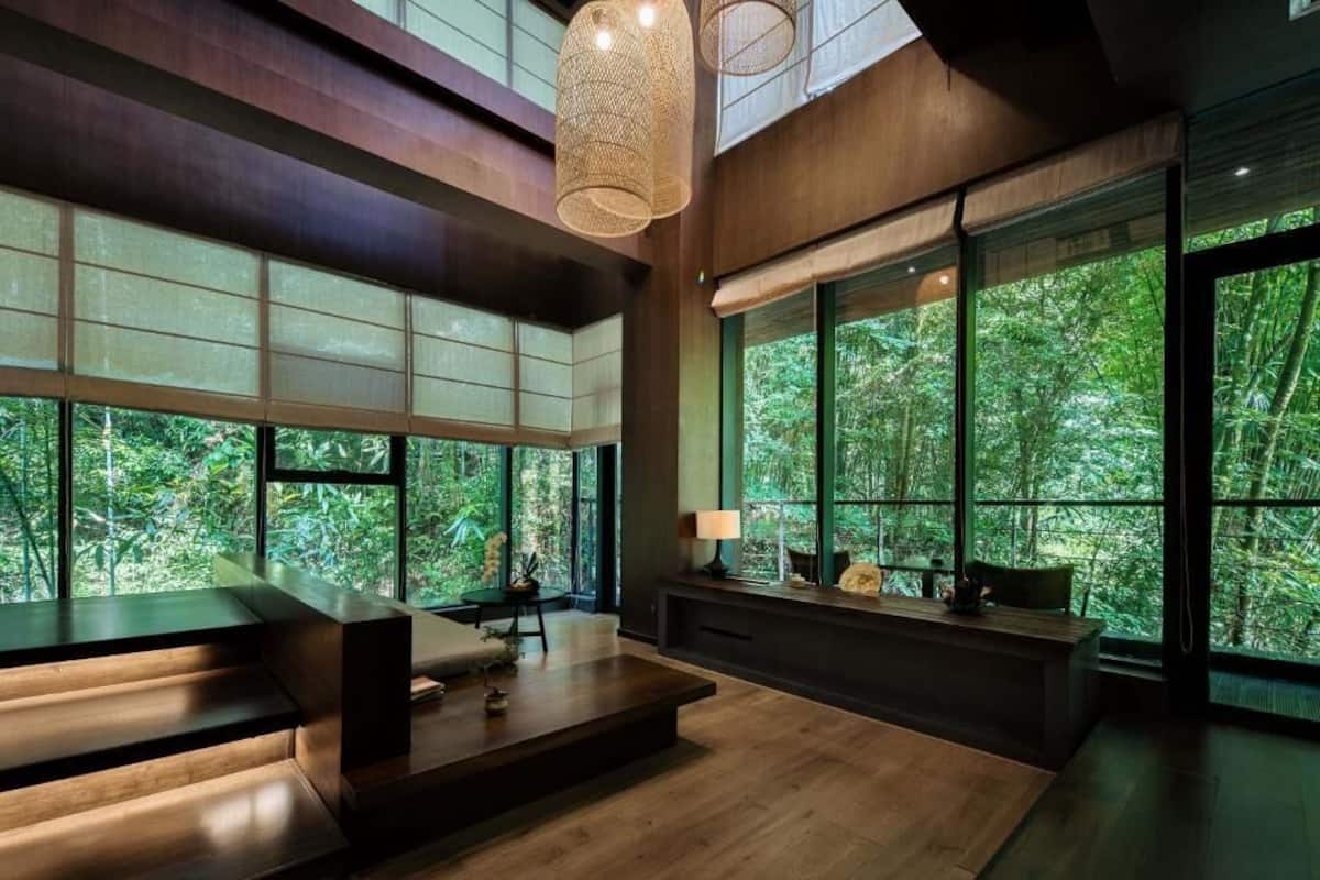 A modern interior with large windows, a wooden bench, and a table with a lamp.