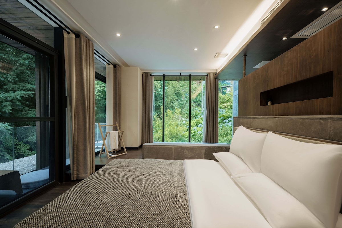 A modern interior with a sofa, large windows, and a view of greenery.