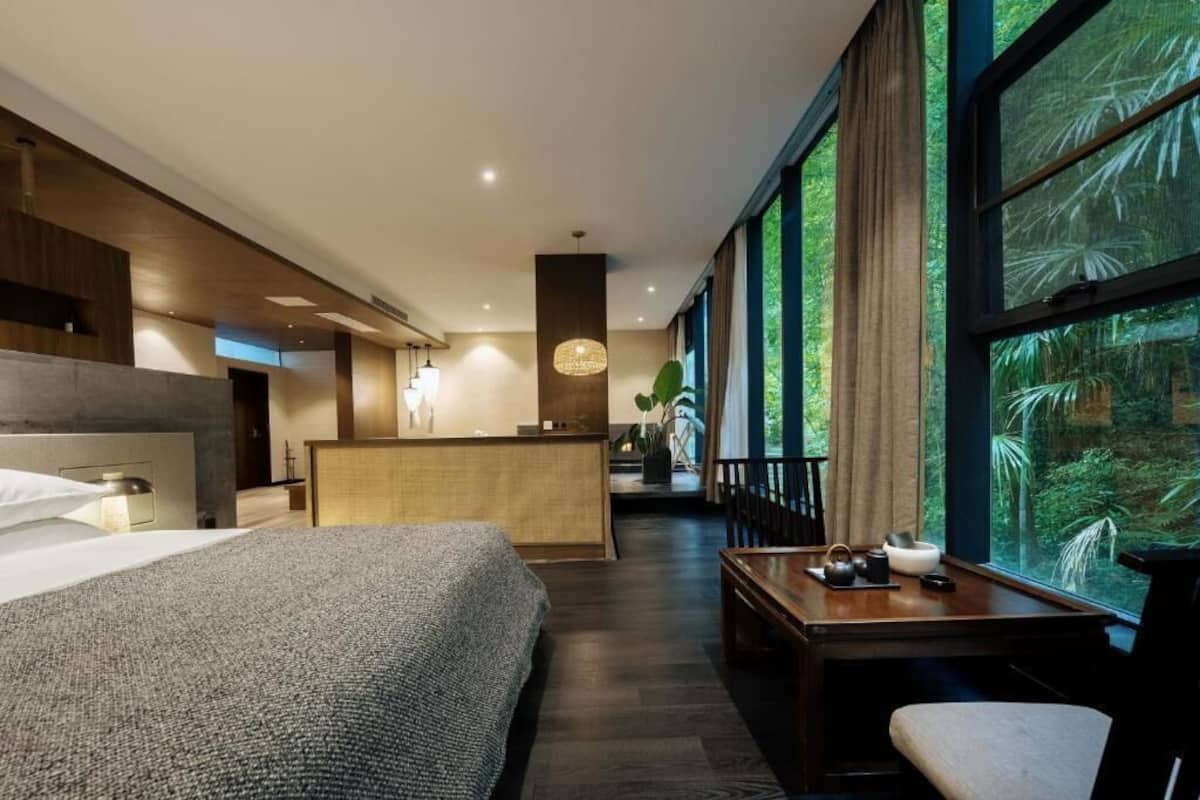 A modern hotel room with a large bed, a desk with a view, and a reception area.