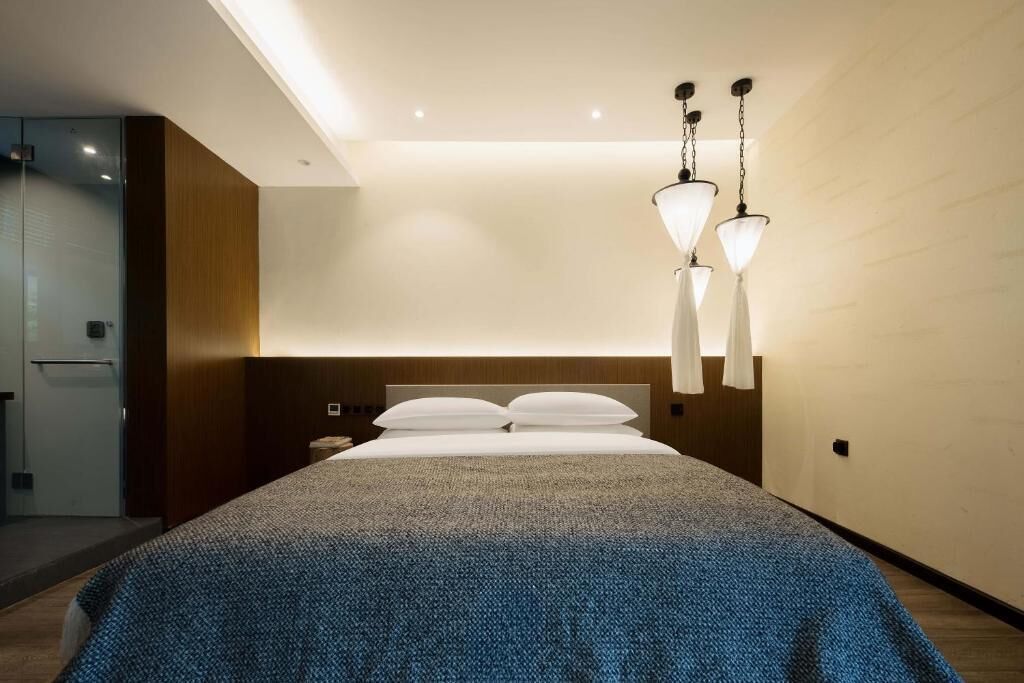 A modern hotel room with a large bed, a wooden headboard, and pendant lighting.