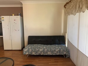 A room with a bed, a white refrigerator, and a window with curtains. - Cozy 1-bedroom (Heathridge)