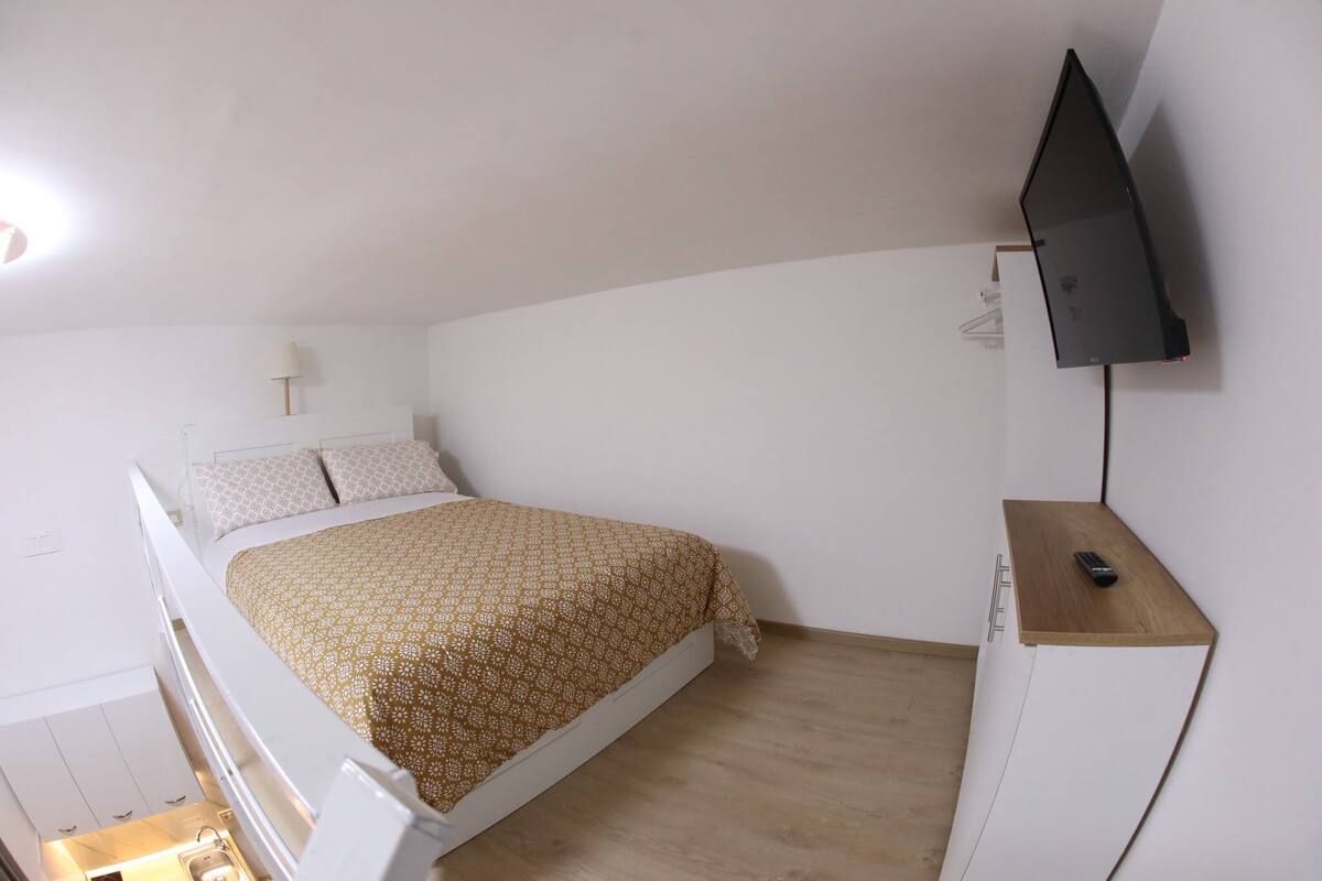 Un dormitorio con cama, televisor montado en la pared y escritorio de madera.