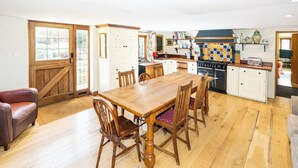 Une cuisine avec des meubles de rangement en bois, une table à manger, des chaises et un fourneau.