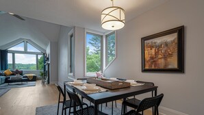 A dining area with a table set for four, a painting on the wall, and large windows. - Huntsville Lakeview Retreat | Jacuzzi & Games (Huntsville)