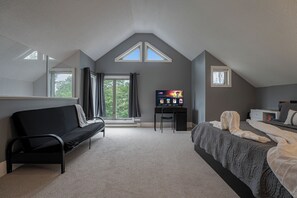 A bedroom with a bed, a desk, a chair, a TV, and a window.