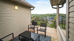 A balcony with a view of a lake and forest, wooden deck, and two chairs and a table. - Huntsville Lakeview Retreat | Jacuzzi & Games (Huntsville)