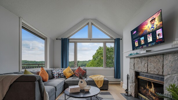 A living room with a fireplace, a large TV, and a view of the outdoors. - Huntsville Lakeview Retreat | Jacuzzi & Games (Huntsville)