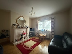A living room with a fireplace, a television, a sofa, and a window with curtains.