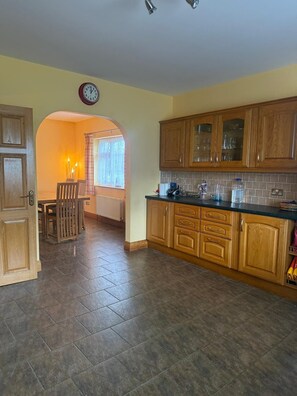 A kitchen with wooden cabinets, a tiled floor, and a dining area with chairs and a table.