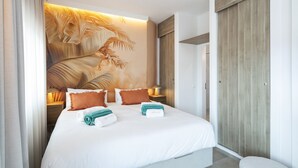 Habitación de hotel con una cama grande, dos almohadas, una mesita de noche, un mural en la pared y un armario de madera.