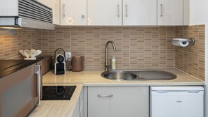 Una cocina moderna con armarios blancos, un lavamanos de acero inoxidable, horno empotrado y un refrigerador compacto.