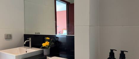 Un baño moderno con un lavamanos blanco, encimera negra y un inodoro. Se ven dos botellas de champú y crema corporal a la derecha.