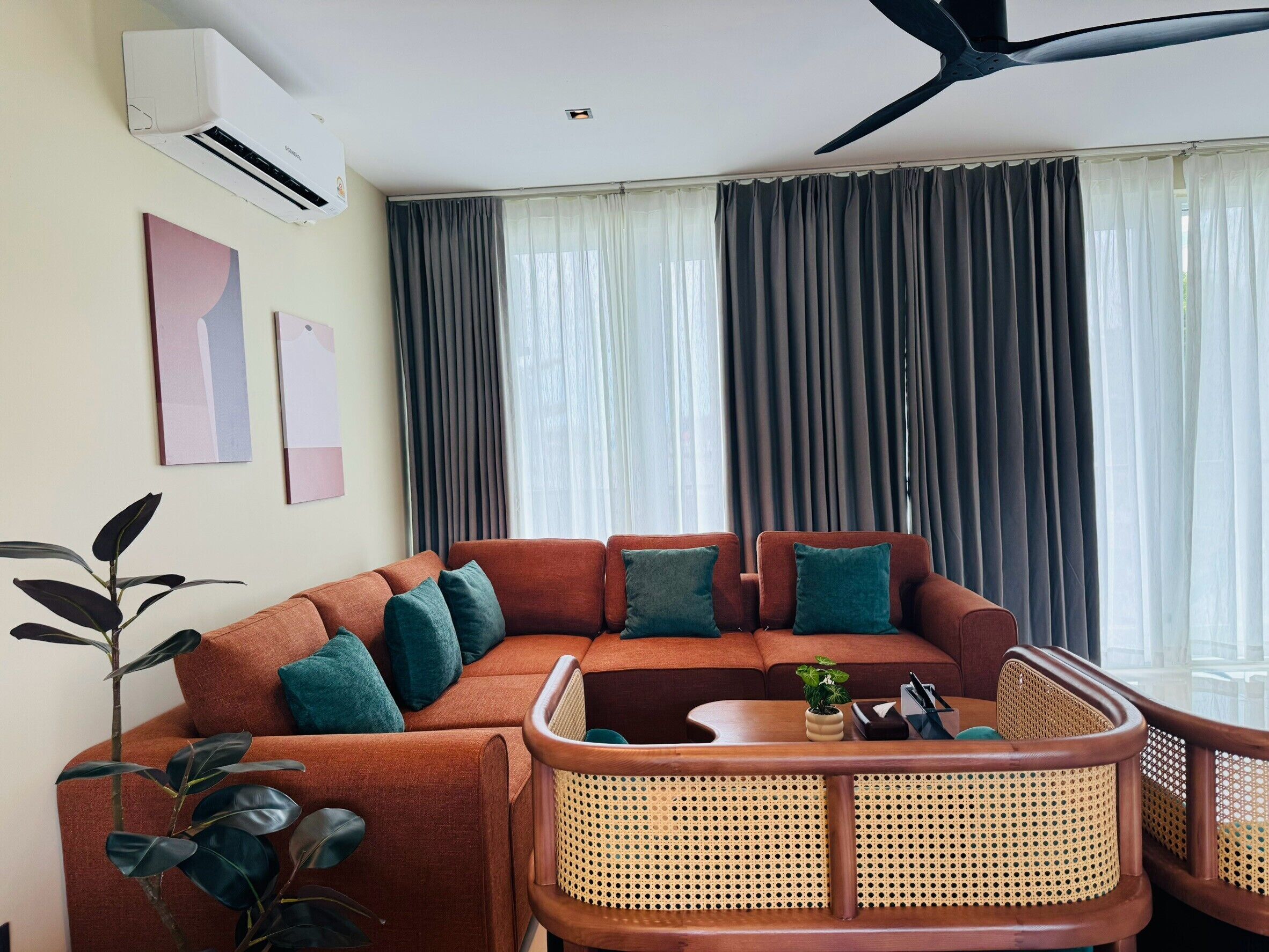 A modern living room with a sectional sofa, a rattan chair, and a ceiling fan.