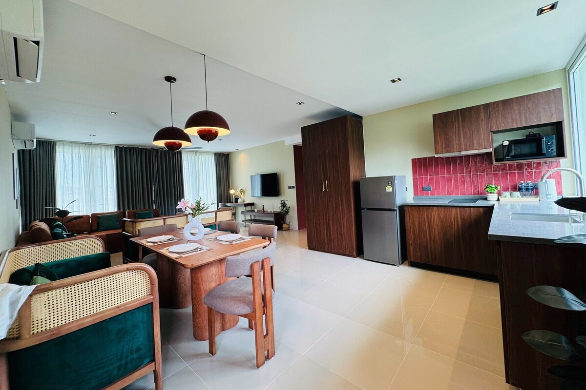 A modern living room with a dining area, kitchen, and a flat-screen TV.