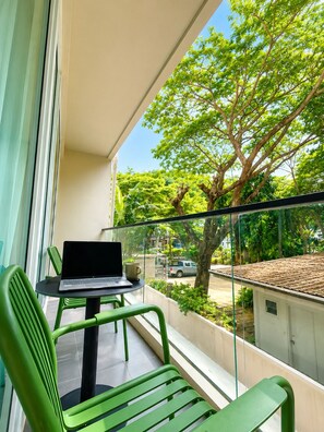 A balcony with a laptop on a table, green chairs, and a view of a tree and parked car. - Syama Mansion Kamala (Kamala)