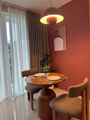 Un comedor con una mesa redonda, sillas, una planta en maceta y una lámpara colgante.