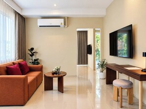 A modern living room with a sofa, coffee table, TV, and a desk with a chair. - Syama Mansion Kamala (Kamala)