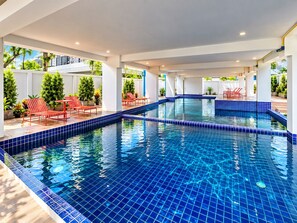 En swimmingpool med blå fliser, omgivet af røde liggestole og krukker med planter.