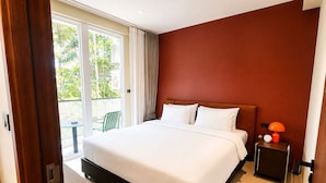 Habitación de hotel con cama, mesita de noche, lámpara y vistas al exterior.