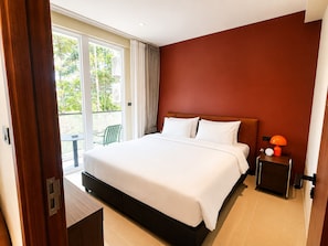 Habitación de hotel con cama, mesita de noche, lámpara y vistas al exterior.