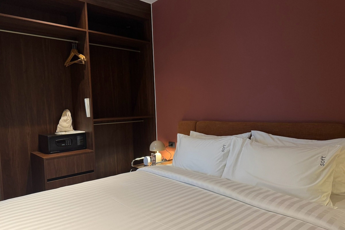 A hotel room with a bed, a wardrobe, a bedside table with a lamp, and a wall-mounted telephone.