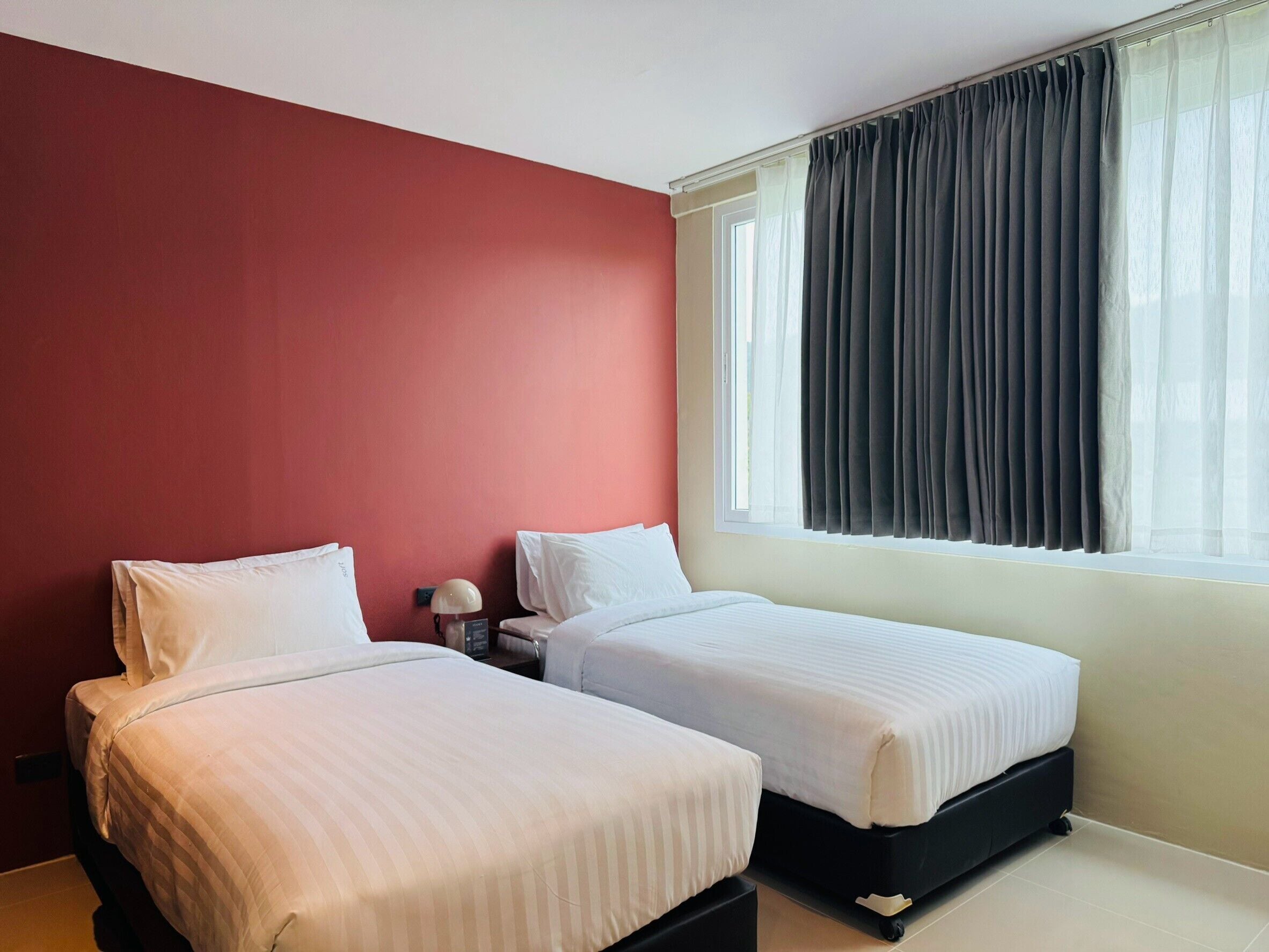 A hotel room with two beds, a nightstand, a lamp, and a window with curtains.
