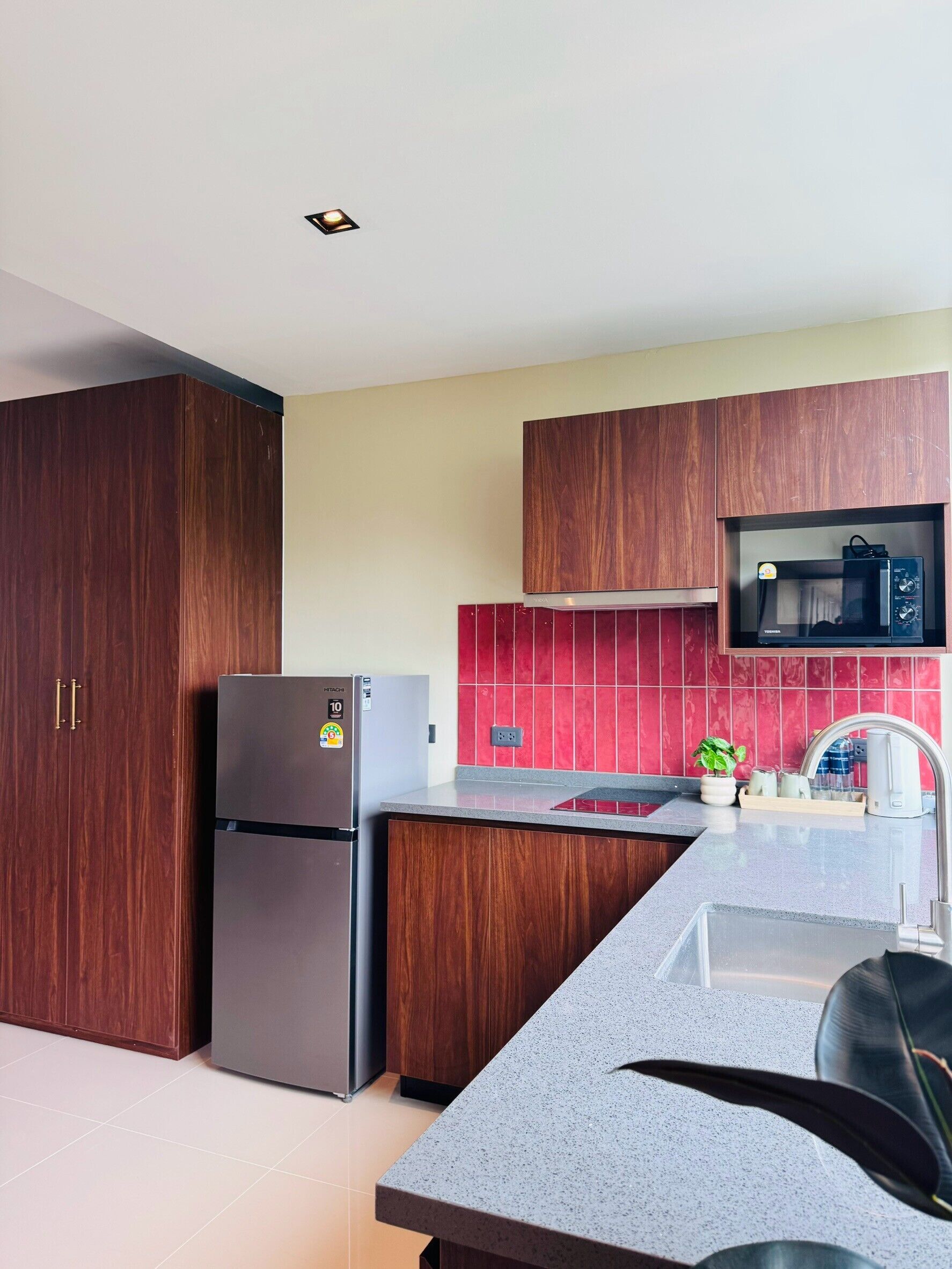 Eine moderne Küche mit Holzschränken, einem Edelstahlkühlschrank, einer Mikrowelle und einer roten Fliesenrückwand.