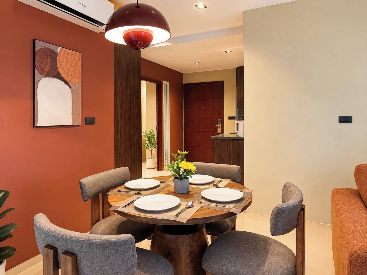 A dining area with a round table, grey upholstered chairs, a central vase with flowers, and a pendant light above.