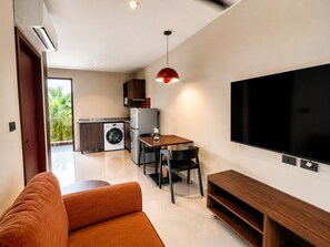 Un espacio habitable moderno con un sofá, un comedor con sillas, una lavadora, un refrigerador y un televisor de pantalla plana grande montado en la pared.