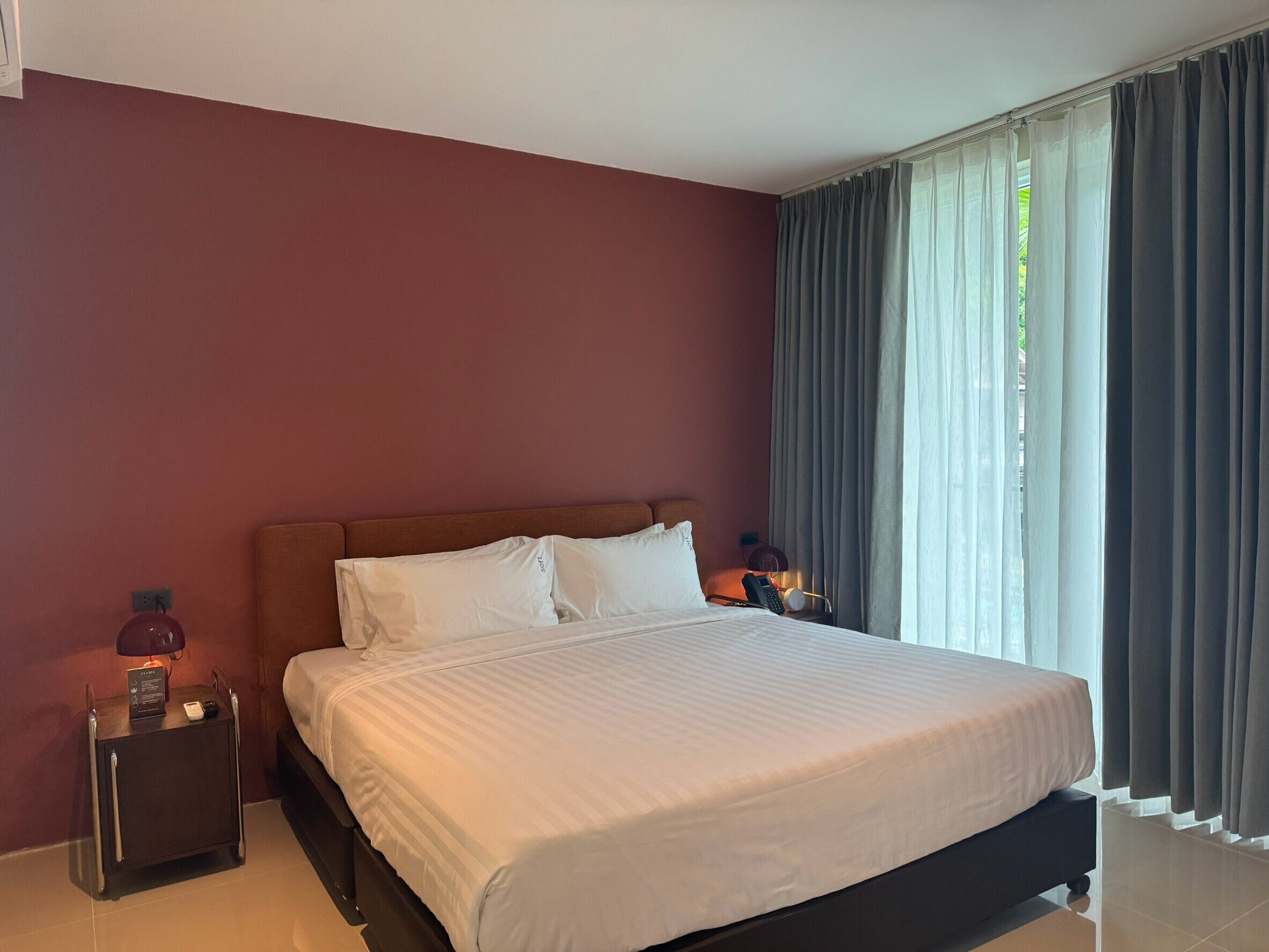 Ein Hotelzimmer mit einem großen Bett, zwei Nachttischen, einem Beistelltisch und einem Fenster mit Vorhängen.