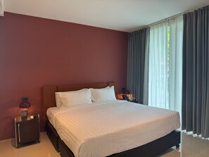 A hotel room with a large bed, two bedside tables, a nightstand, and a window with curtains. - Syama Mansion Kamala (Kamala)