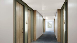 Un couloir avec des portes en bois, un sol recouvert de moquette et une vue sur la verdure par une fenêtre.