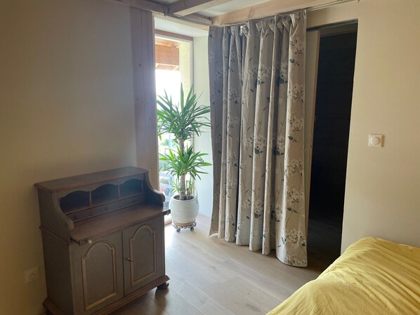 A room with a wooden cabinet, a potted plant, a bed, and a door with curtains.