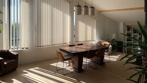 Un'ampia sala da pranzo con tavolo e sedie in legno, grandi finestre con persiane verticali e lampadari a sospensione.