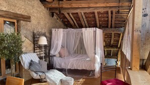 Una camera da letto rustica con un letto a baldacchino, un tavolo di legno, una sedia e uno sgabello.