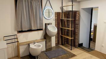 Een moderne badkamer met een bidet, een spiegel, een plank en een raam met gordijnen.