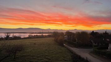 Ländliche Landschaft mit einer Straße, Häusern und einem Sonnenuntergang über Bergen.