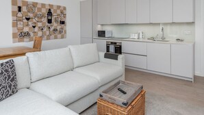 Un salon moderne avec un canapé, une table basse et un coin cuisine doté de meubles blancs et d’appareils électroménagers.