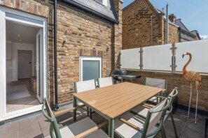 Eine Terrasse mit Holztisch und -stühlen, einem Grill und einer Flamingostatue.