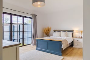 A bedroom with a large window, a bed, a bedside table, and a nightstand. - Converted Barn with Oak Beams near Cotswolds (Highworth)