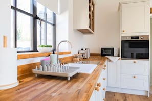 A modern kitchen with a wooden countertop, a built-in sink, and white cabinetry. - Converted Barn with Oak Beams near Cotswolds (Highworth)