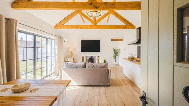 Ein modernes Interieur mit Holzbalkendecke, einer Couch, einem Fernseher und einem Essbereich.