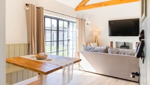 Ein modernes Zimmer mit einem Holztisch, einer Couch, einem Fernseher und einem Fenster mit Vorhängen.
